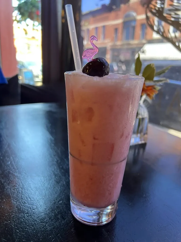 creamy pink drink served in a highball glass, topped with a dark cherry and a flamingo pick.